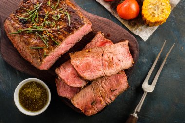 Üzerinde kesme tahtası ızgara sebzeli biftek dilimlenmiş. Üstten görünüm.