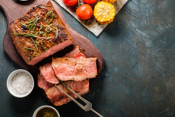 Sliced Roast beef on cutting board with grilled vegetables. Top view. Copyspace.