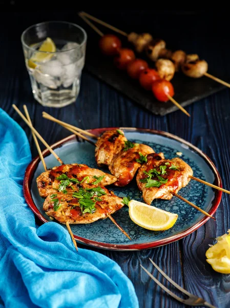 Chicken kebab on skewers with cherry, mushrooms and barbecue sauce on a blue background.