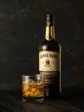 Minsk; Beyaz Rusya-Temmuz 3, 2018: Şişe Jameson Caskmates İrlanda viski ve cam buz üzerine ahşap arka plan ile. Jameson Pernod Ricard İrlandalı Distillers iştiraki tarafından üretilen karma bir İrlanda viski olduğunu.