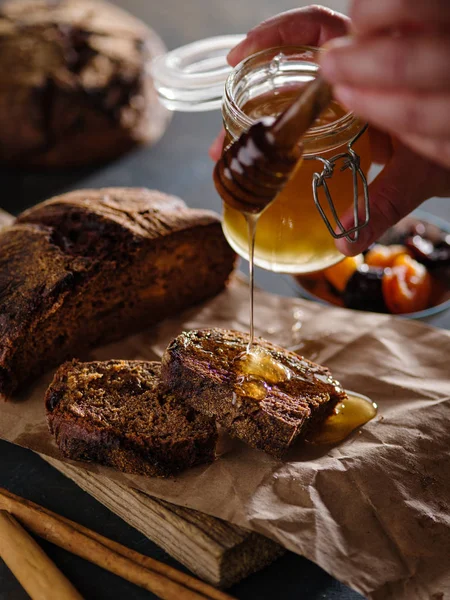 A girl is pouring honey on the bread. Homemade rye bread with prunes and dried apricots