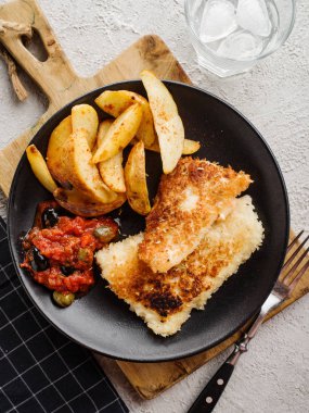 Domates-zeytin sosu ve patates ile kızarmış balık, üst görünümü.