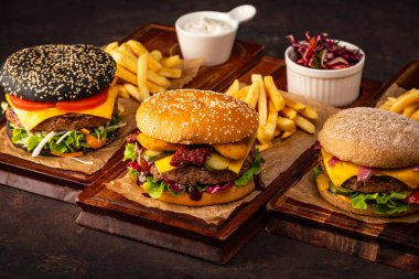 Ahşap Tahtada Üç Sulu Ev Yapımı Beef Cheeseburger. Koyu bir arka plan üzerinde sığır eti ve peynir ile hamburger çeşitleri.