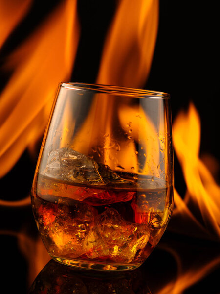 Glass of whiskey with ice on a background of fire
