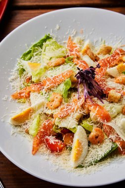 Ahşap masada Peynirli Deniz Ürünleri Salatası. Beyaz tabakta Karidesli Somon Salatası.