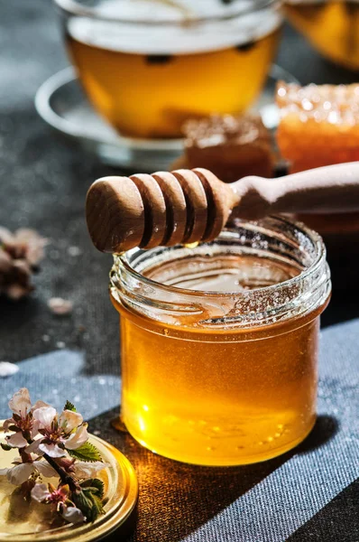 Ein Glas Honig mit Waben und einem Stock, eine Teekanne mit einer Tasse — Stockfoto