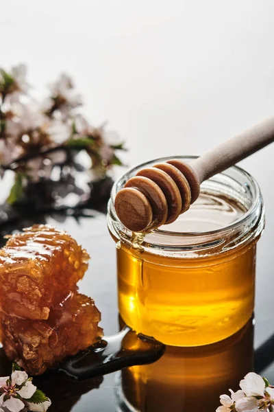 Un borcan de miere cu fagure de miere și un băț pe un fundal ușor — Fotografie, imagine de stoc