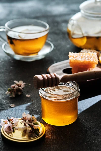 Ein Glas Honig mit Waben und einem Stock, eine Teekanne mit einer Tasse — Stockfoto