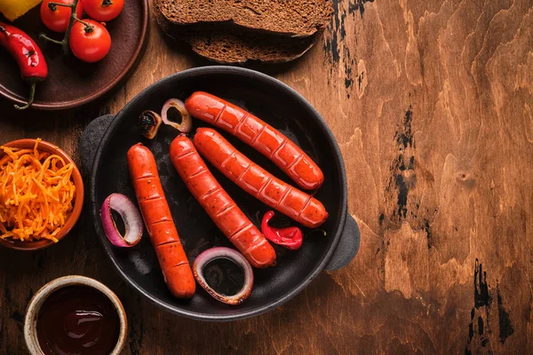 Salsichas grelhadas em uma panela com cebolas e legumes — Fotografia de Stock