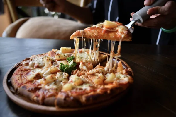 Domates sosu, peynir ve ananas ile süslenmiş pizza, tahta masanın üzerinde ahşap tabakta servis edilir. Hawaii pizzası fotoğrafı. Dilimlenmiş pizza.