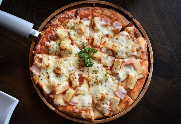 Domates sosu, peynir ve ananas ile süslenmiş pizza, tahta masanın üzerinde ahşap tabakta servis edilir. Hawaii pizzası fotoğrafı.