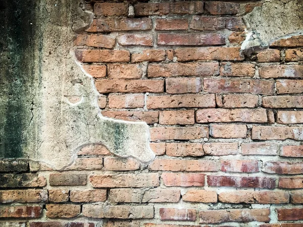 An aged, cracked and chipped stucco wall with an area of exposed brown brick. Brick wall background texture and wallpaper. Wall decoration and design.