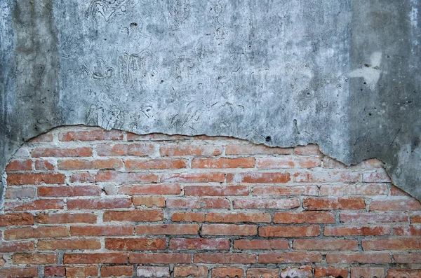 An aged, cracked and chipped stucco wall with an area of exposed brown brick. Brick wall background texture and wallpaper. Wall decoration and design.