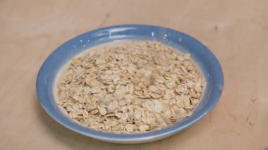 Yuvarlanmış yulaf ezmesi ve tabak maketi. Yulaf taneleri tabağa dökülüyor. 4k video görüntüsü.