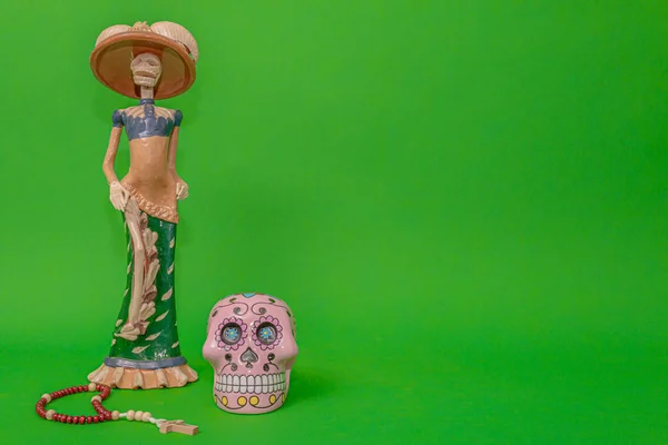 Calavera de la Catrina heykelciğinin yanında ahşap bir tespih ve pembe bir kafatası.