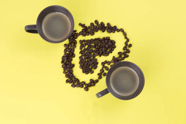 Coffee beans in the shape of the heart with two cup of coffee on the yellow background