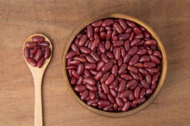 Ahşap arka plan üzerinde kırmızı fasulye ahşap kase ve kaşık üstten görünüm.