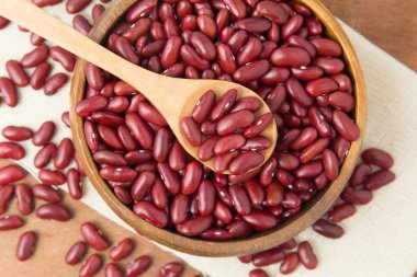 Ahşap kase ve keten ve ahşap zemin üzerine koyarak kaşık kırmızı fasulye.