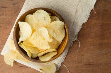 Patates cipsi ahşap kase keten ve ahşap zemin üzerine koyarak üstten görünüm.