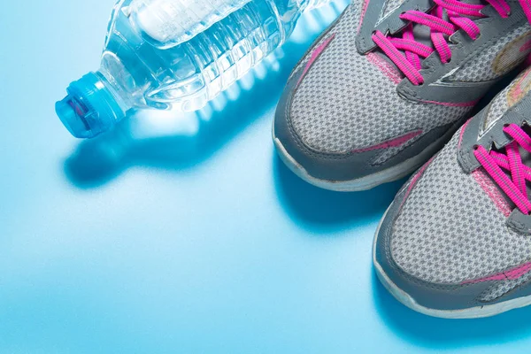 Sport pink shoes and bottle of water on blue background with copyspace for your text. Concept healthy lifestyle and diet.