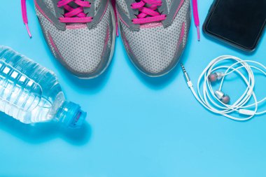 Spor düz pembe ayakkabı şişe su, telefon, kulaklık boşaltmak mavi zemin üzerine yatırın. Kavram sağlıklı yaşam tarzı ve diyet.