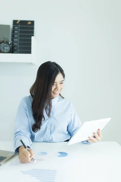 Young asian business woman using tablet for working at desk in office with documents and laptop.