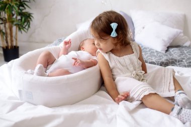 2 yaşındaki güzel kız kardeş, yeni doğan erkek kardeşine bakıyor. Yatak odasında, yatak odasında yatıyor.