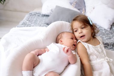 2 yaşındaki güzel kız kardeş, yeni doğan erkek kardeşine bakıyor. Yatak odasında, yatak odasında yatıyor.