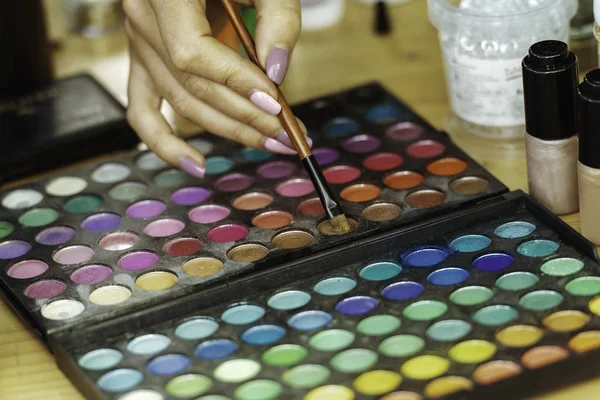 Women makeup artist hand reaching for colour in palette.