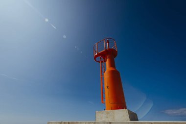 Küçük modern kırmızı deniz feneri direği yenilenmiş beton köstebek mavi gökyüzünde izole.