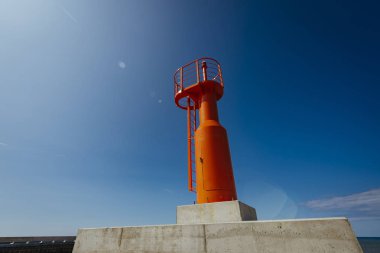Küçük modern kırmızı deniz feneri direği yenilenmiş beton köstebek mavi gökyüzünde izole.