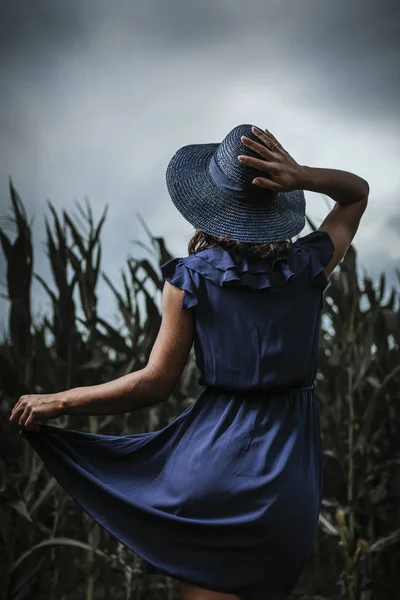 Fırtınalı bulutlar sırasında mısır tarlasında arkadan mavi şapkalı güzel bir kadın..