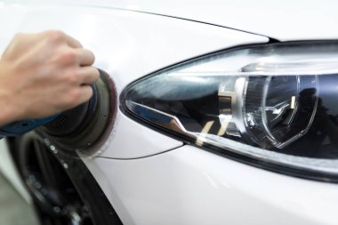 Bir adam, arabanın boyalı yüzeyini hava geçirmez cilalama makinesiyle cilalıyor.