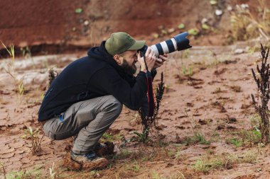 Kamerayı uzun objektifle tutan ve güneşli bir sonbahar gününde dışarıda fotoğraf çeken bir adam..