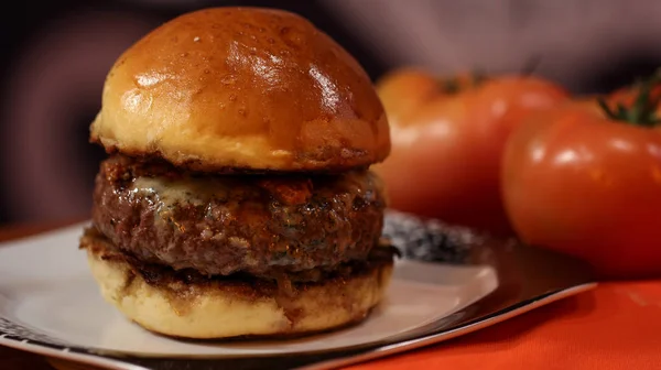 Arkada domates olan bir tabakta büyük hamburger