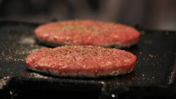 İki hamburger köftesi siyah metal ızgara tuz ve biber ızgara ile terbiyeli