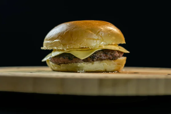 Cheeseburger simples em uma placa de madeira fundo preto — Fotografia de Stock