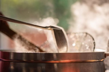 Lokantadaki şef büyük bir tencerede kepçeyle yemek pişiriyor. Su kaynıyor ve buhar kütlesi sabah ışığında yansıyor..