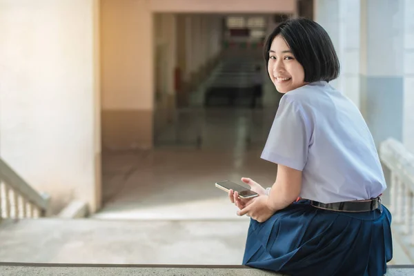 아시아 여학생 제복을 앉아서 얼굴을 돌리고 웃으며 계단에 있습니다 — 스톡 사진