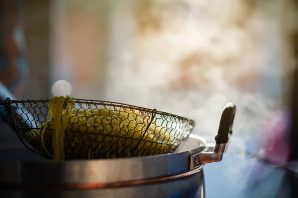 Restoranda yemek pişiren kişi büyük bir tencerede sarı erişte pişirmek için elek kullanırken yemek pişiriyor. Su kaynıyor, duman var, sıcak tükürük var..