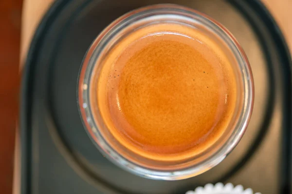 Temiz bir bardakta sıcak espresso kahvesi metal bir tepsiye ve koyu kahverengi ahşap bir masada küçük bir ahşap rafa yerleştirilir..