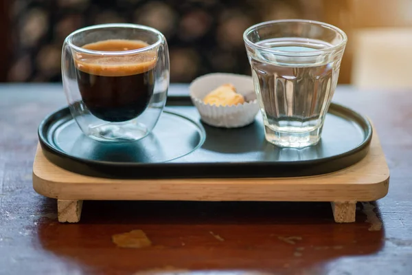 Temiz bir bardakta sıcak espresso kahvesi metal bir tepsiye ve koyu kahverengi ahşap bir masada küçük bir ahşap rafa yerleştirilir..