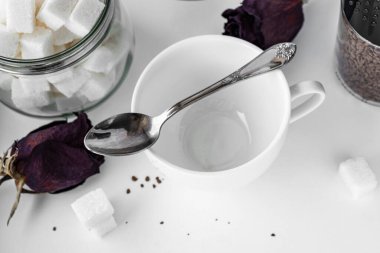 Üzerinde çay kaşığı olan boş bir bardak. Kupanın yanında bir kutu kahve ve rafine şeker var.
