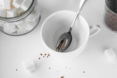 İçinde çay kaşığı olan beyaz bir kupa. Bir kavanoz rafine şeker ve bir kavanoz granüllü kahvenin yanında.