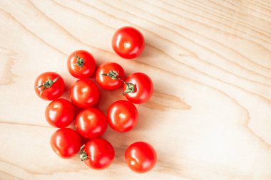 Kiraz rengi domatesler açık tahta bir tahtanın üzerinde duruyor.