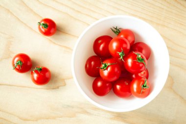 Tahtanın üzerinde beyaz bir kase içinde kiraz domatesleri. Kasenin yanında üç kirazlı domates var.