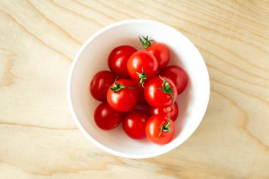 Tahtadaki küçük beyaz kasede kırmızı kiraz domatesleri.