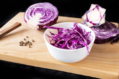 Açık ahşap bir tahtanın üzerinde, koyu beyaz bir kasede öğütülmüş mor lahana. Kâsenin yanında, yarım lahana ve karabiber.