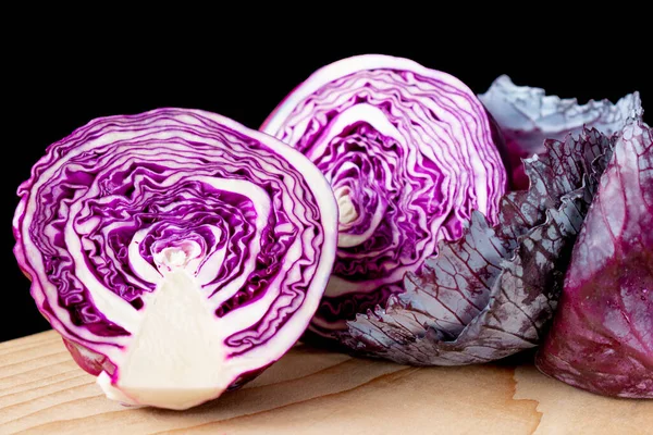 Purple cabbage cut in half on a wooden Board along with cabbage leaves