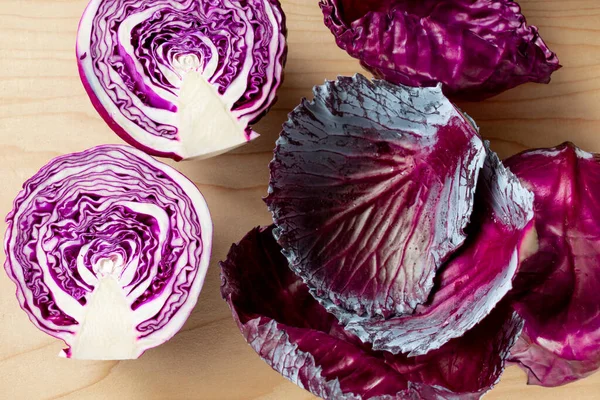 Purple cabbage cut in half on a wooden Board. Nearby are cabbage leaves